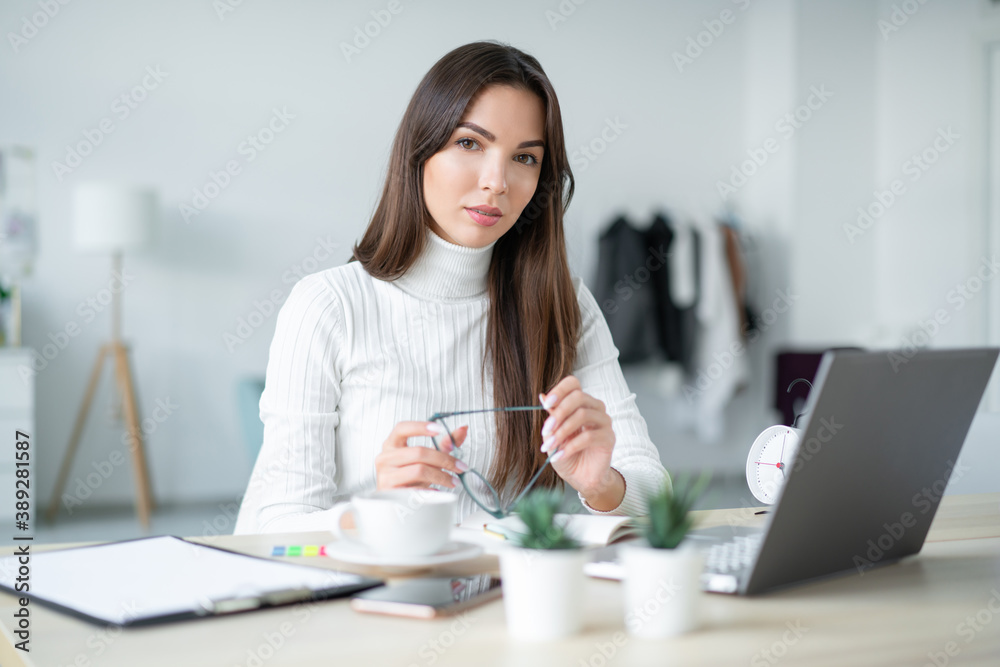 Young business woman sits table in front of aptop and holds glasses in her hands. Young business woman sits table in front of aptop and holds glasses in her hands.
