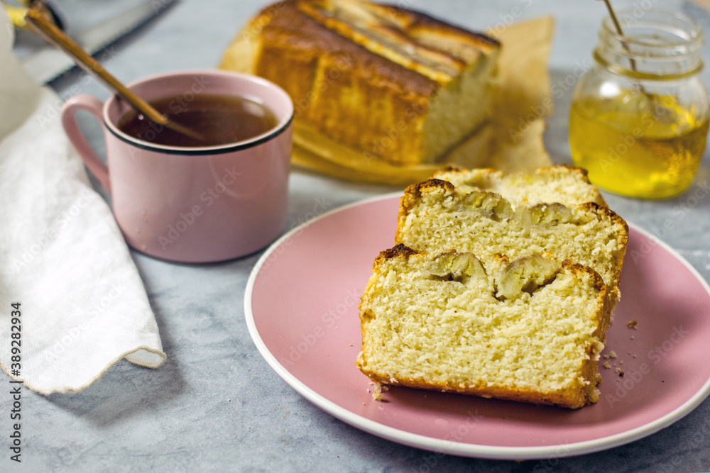 Banana cake gluten free and sugar free for breakfast. Pieces of banana bread on a pink plate on a gray table, next to a cup of tea, honey. Healthy nutrition concept Banana cake gluten free and sugar free for breakfast. Pieces of banana bread on a pink plate on a gray table, next to a cup of tea, honey. Healthy nutrition concept