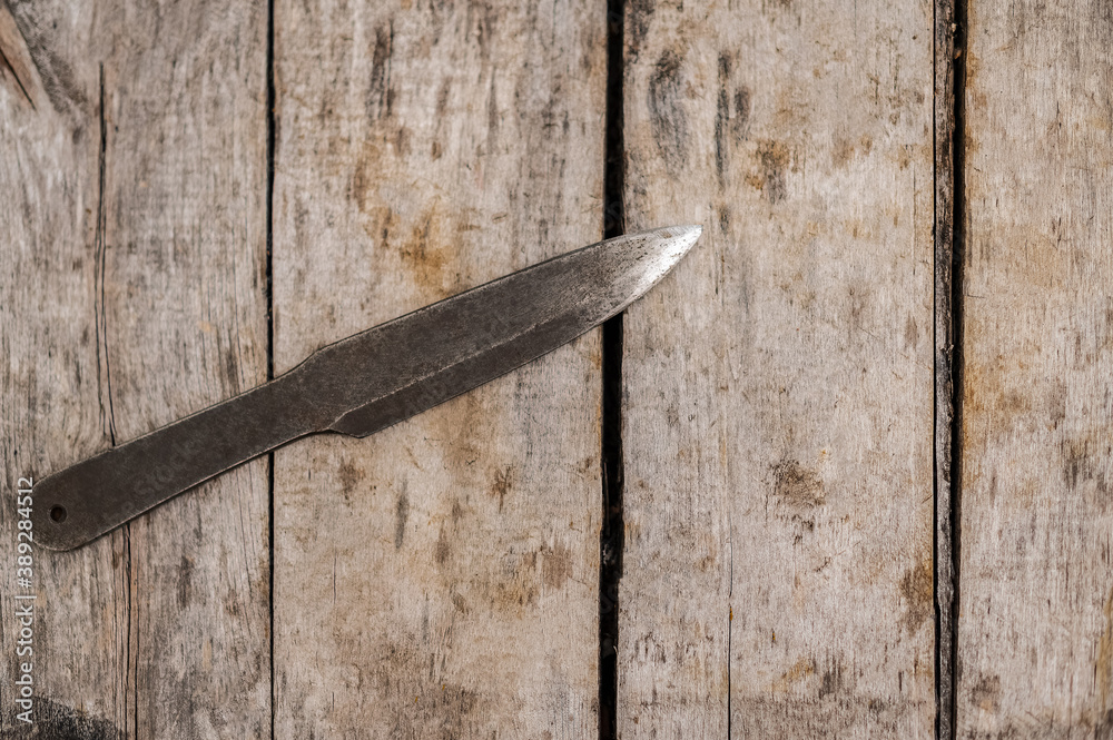 An old rusty throwing knife on old dirty boards.
