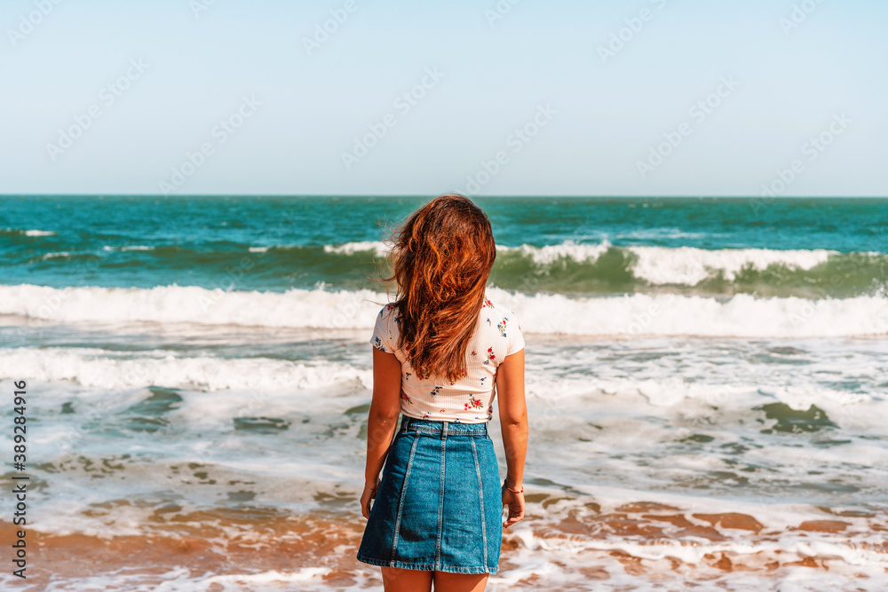 Happy woman with long hair standing on the beach in front of the blue sea or ocean, the concept of the elements and freedom