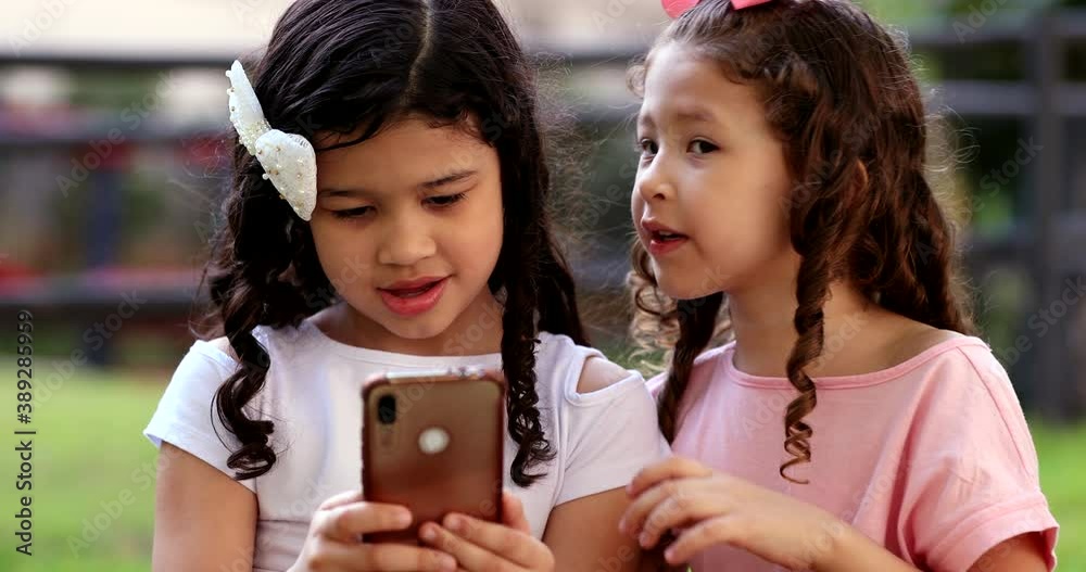 Two mixed race little girls watching media on smartphone outside Two mixed race little girls watching media on smartphone outside