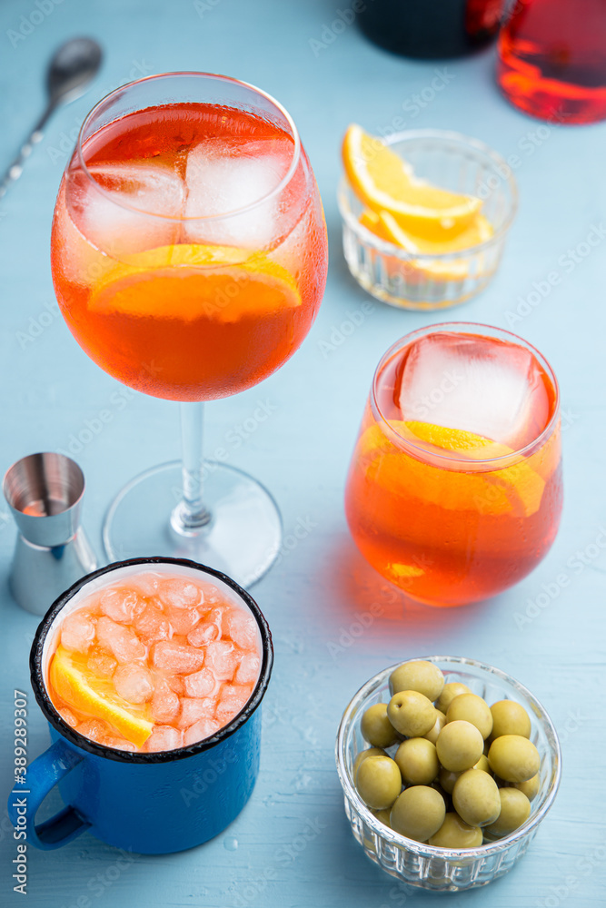 Different glasses of classic italian spritz cocktail with olives on a blue table
