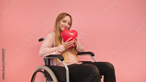 Foto Young caucaian disabled woman in wheelchair holding heart balloon