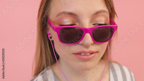 Young caucasian woman with sunglasses listening to the music using headphones . Isolated on pink background, close up. High quality photo © CameraCraft