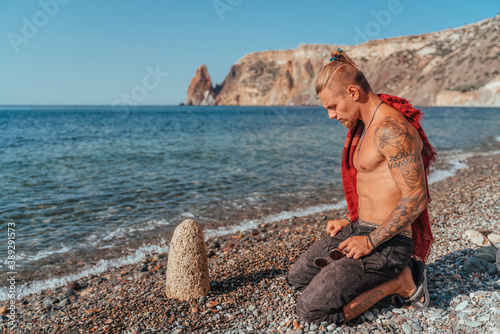 Принти на полотні Mature Tattooed Man sitting on the beach before rock and pray