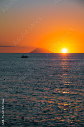 Amazing view of the Stromboli Volcano at sunset, wit the sun going down and amazing sea and sky colors. View form the coast of Calabria, Italy, in the touristic destination of Tropea. © laura