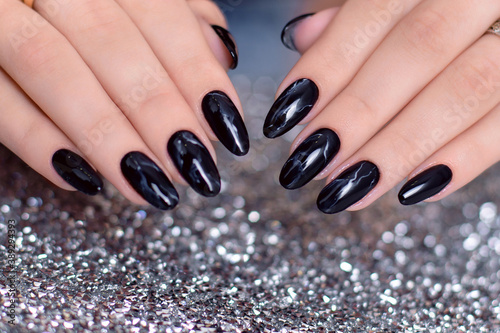 Beautiful female hands with fashion manicure nails, black gel polish, on glitter background photo
