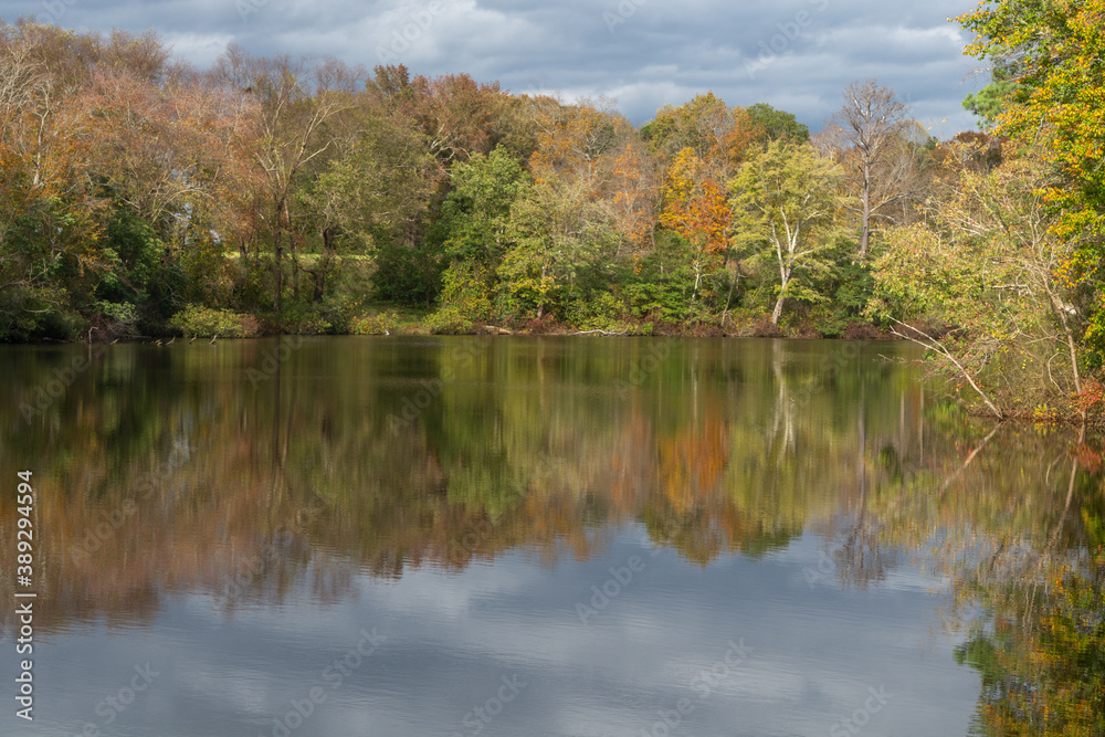 Reflection of fall trees on a lake. Beautiful cloudy fall day at the lake with colors of fall leaves reflecting on the river.