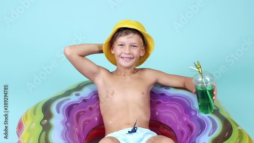 Cute little boy with cocktail relaxing on inflatable ring against color background