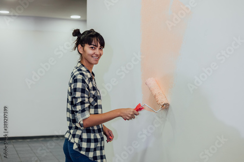 Beautiful girl painting the wall with a roller. Interior renovation