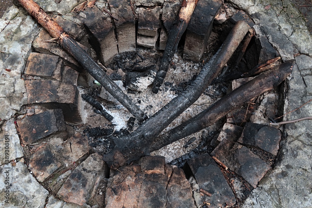 Old circular firepit made of heat resistant bricks, with some large burnt canes and pieces of wood inside. Old circular firepit made of heat resistant bricks, with some large burnt canes and pieces of wood inside.