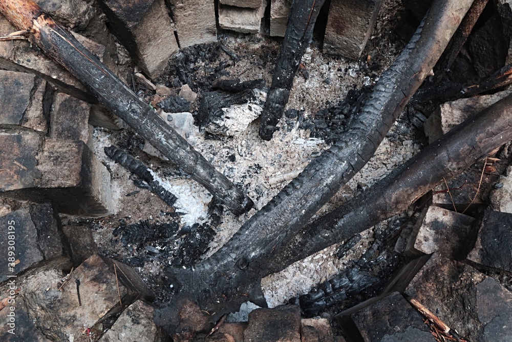 Detail of old circular firepit made of heat resistant bricks, with some large burnt canes and pieces of wood inside. Detail of old circular firepit made of heat resistant bricks, with some large burnt canes and pieces of wood inside.
