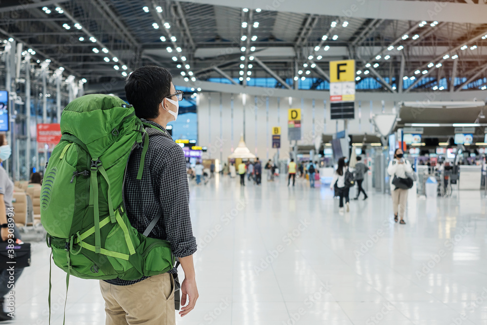Φωτογραφία Young man traveler wearing medical face mask and checking flight time in airport terminal, protection Coronavirus disease (Covid-19) infection