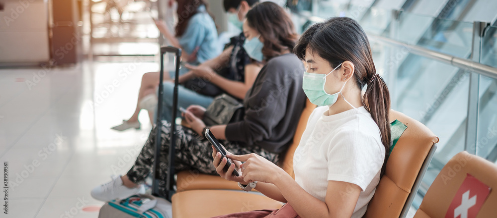 Young female wearing face mask and using mobile smartphone in airport, protection Coronavirus disease (Covid-19) infection, Asian woman traveler sitting on chair. New Normal and social distancing Young female wearing face mask and using mobile smartphone in airport, protection Coronavirus disease (Covid-19) infection, Asian woman traveler sitting on chair. New Normal and social distancing