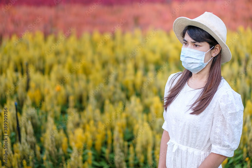 Happy tourist woman wearing surgical face mask  enjoy beautiful Flowers garden, protection Coronavirus disease (Covid-19) infection. New Normal, travel safety, vacation and holiday concept