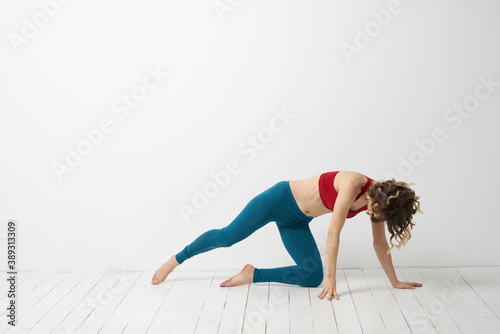 A woman in blue jeans practices yoga on a light background indoors and a slim figure in gymnastics