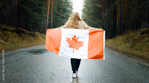 Girl walks through the forest holding the flag of canada. Back view