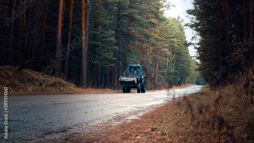 The tractor is driving along the road in autumn. Front view