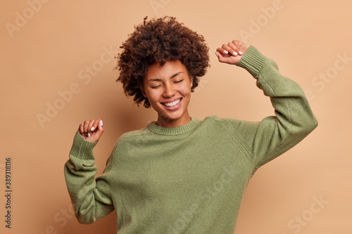 Фотография Horizontal shot of happy curly haired Afro American woman feels lively and dance