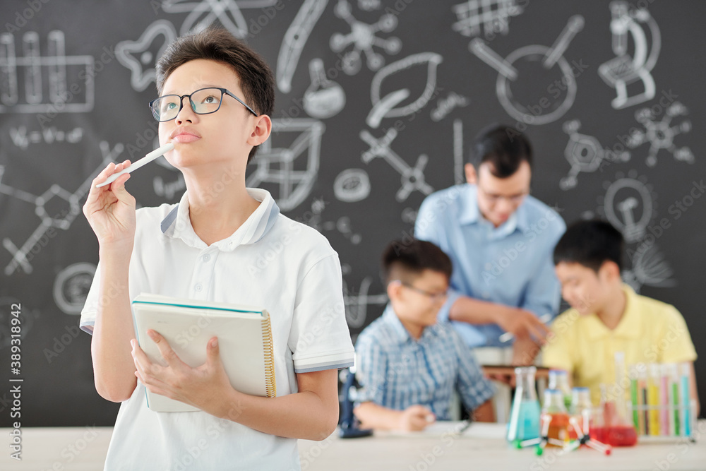 Φωτογραφία Portrait of pensive Vietnamese schoolboy with notebook and pencil looking up whe