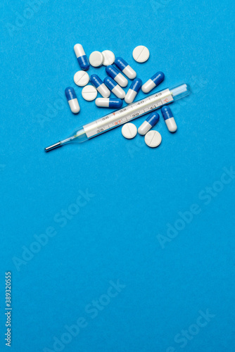 group of white pills or tablets and mercury thermometer on blue background