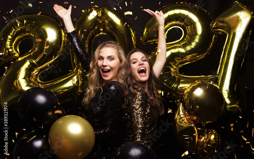 Happy gorgeous girls in stylish sexy party dresses holding gold 2021 balloons, having fun at New Year's Eve Party.