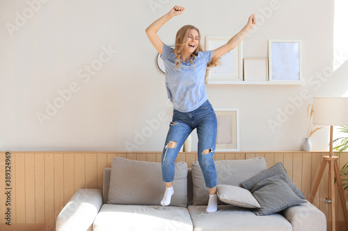 Attractive young woman is having fun at home. Girl is jumping and dancing on sofa. © ty