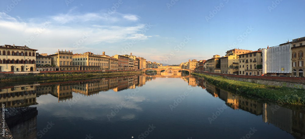 Panoramic image of historic buildings along the the Arno River, reflecting on the still surface of the river