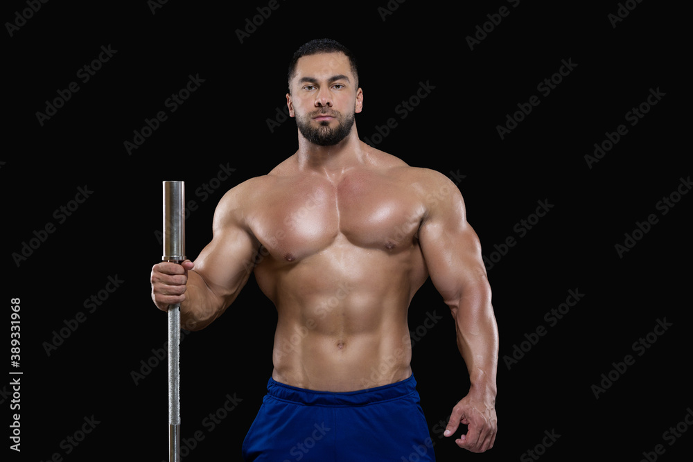 Young sexy athlete man is standing leaning with one hand on the barbell isolated on black background Young sexy athlete man is standing leaning with one hand on the barbell isolated on black background