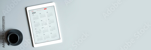 a tablet with an open calendar for 2021 year and a cup of coffee on a gray background. banner. space for text