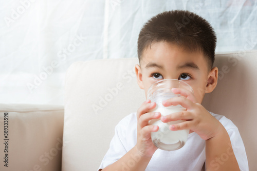 Close up of happy Asian little cute child boy hand holding milk glass he drinking white milk during sitting on the sofa at home after lunch. Daily life health care Medicine food