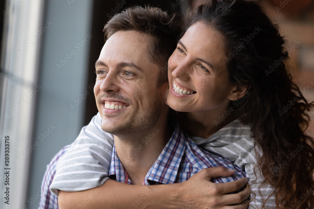 Obraz premium Close up of excited young Caucasian couple hug look in distance dreaming or thinking happy bright future together. Smiling man and woman imagine visualize new perspectives. Vision, marriage concept.