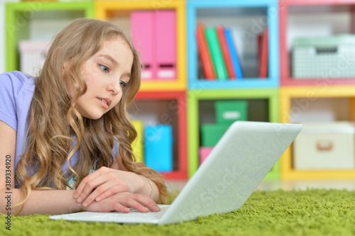 Cute girl using laptop while lying on green floor at home