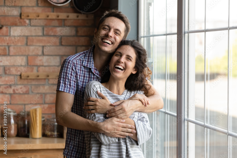 Portrait of overjoyed millennial man and woman hug cuddle excited to move to new own shared apartment together. Smiling young Caucasian couple embrace enjoy family weekend at home. Rental concept. Portrait of overjoyed millennial man and woman hug cuddle excited to move to new own shared apartment together. Smiling young Caucasian couple embrace enjoy family weekend at home. Rental concept.