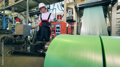 Factory machine is producing polyethylene foil under worker's control