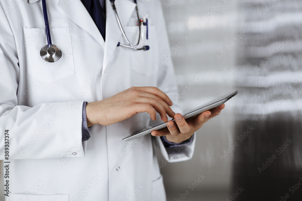 Unknown male doctor using tablet computer in clinic near his working place, closeup. Perfect medical service in hospital. Medicine and healthcare concept Unknown male doctor using tablet computer in clinic near his working place, closeup. Perfect medical service in hospital. Medicine and healthcare concept