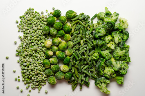 A mix of frozen green vegetables: beans peas broccoli Brussels sprouts on white
