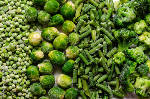 A mix of frozen green vegetables: beans peas broccoli Brussels sprouts on white background.
