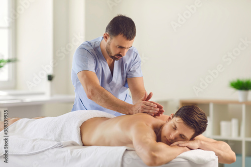 Serious masseur doing relaxing back massage for young man using Tapotement technique