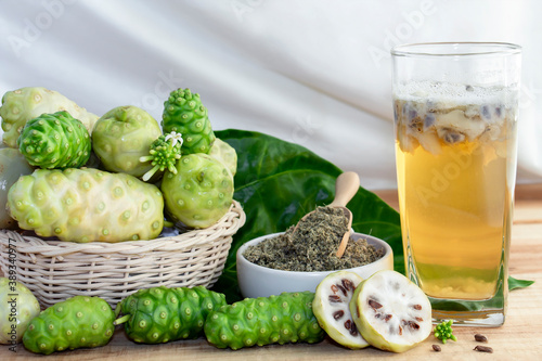 Noni fruit juice or Morinda Citrifolia and leaves of noni in basket on the wooden table background, it is good source of vitamin edible and delicious for healthy.