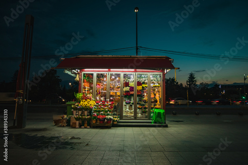 Fototapeta Naklejka Na Ścianę i Meble -  Roadside flower shop during night time. Lonely flower shop late at night, with flowers visible blooming under neon lights.