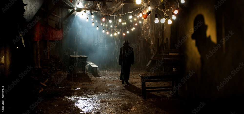 Silhouette of a man in a coat and hat in a dark alley on a rainy night. theme of violence and cruelty