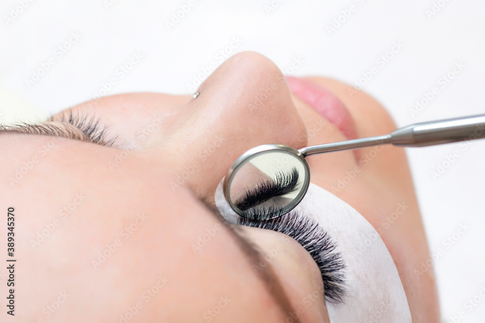 Fototapeta premium Eyelash extension procedure. Female eye with long eyelashes. Close up. mirror in the hands