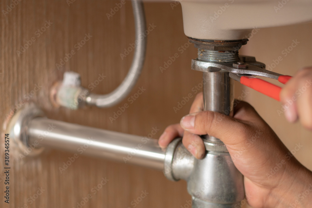 Plumber repairs and maintains chrome siphon under the washbasin in bathroom. Maintanance home ideas concept. Selective focus and freespace for background. Plumber repairs and maintains chrome siphon under the washbasin in bathroom. Maintanance home ideas concept. Selective focus and freespace for background.