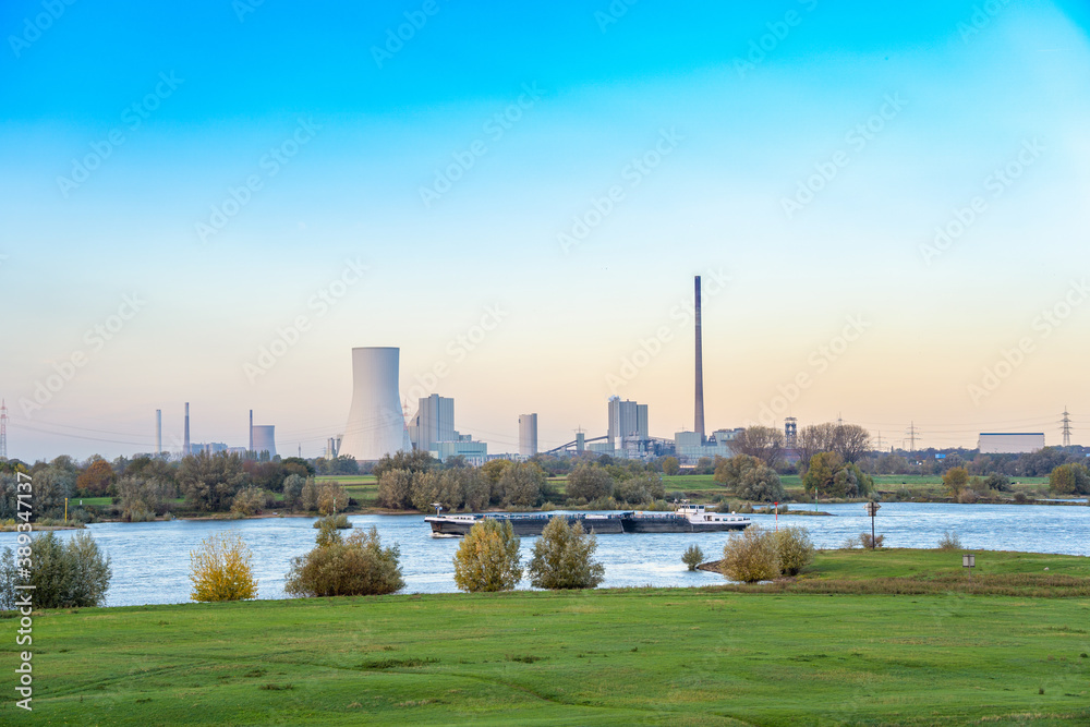 Landschaft am Rhein mit einem Binnenschiff und großem Kraftwerk im Hintergrund