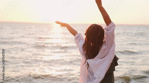 beautiful girl dancing on the beach in a white shirt. Free girl with long hair in a white shirt dances in the sunset. Healthy woman dancing on the beach.