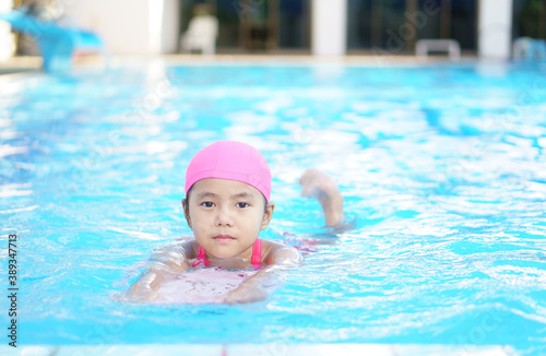 Asian child cute or kid girl smile wearing swimming suit on school swimming pool and happy fun in water park for learn and training swim on kick board or refreshing relax to exercise on summer holiday