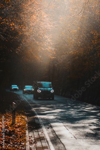 Cars driving on a early morning with dramatic lightrays form the sunrise in the mountains with foggy atmosphere. Mountain road in the Harz National Park in Germany
