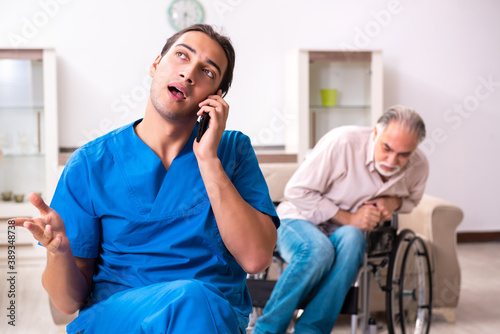 Valokuva Old man in wheel-chair and young bad caregiver indoors