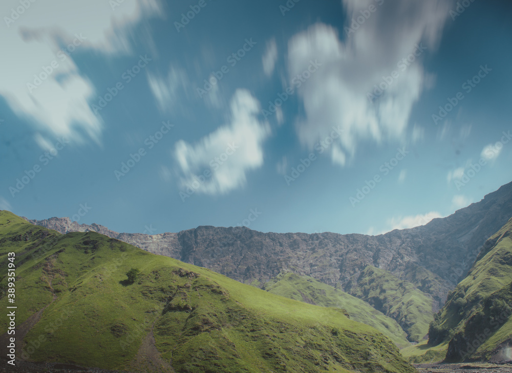 Fototapeta premium Nice hills covered by green grass above them clouds in blue sky. behind them rocks .